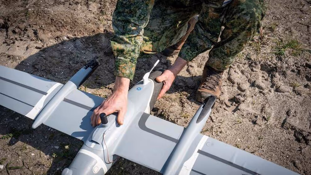 Gehurkte militair werkt aan drone die op de grond ligt.