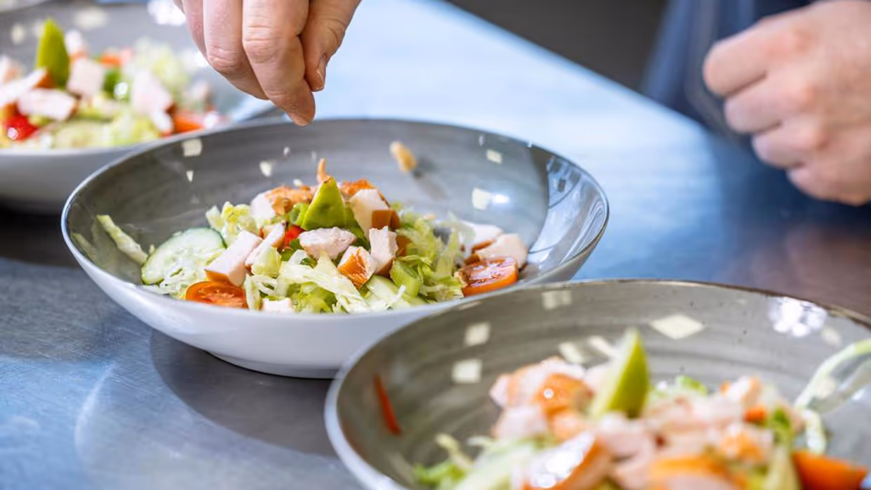 Een hand strooit iets over een bord met eten.