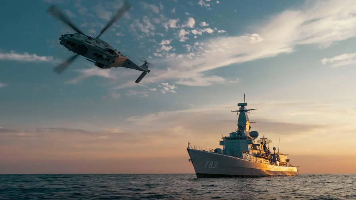Een fregat op zee, terwijl een marinehelikopter voorbijvliegt.