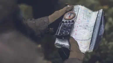 Een militair kijkt op een landkaart en gebruikt zijn kompas.