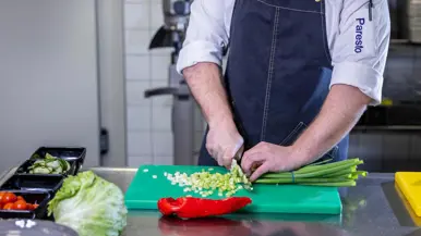 Op de linkerfoto een mooi opgemaakt bord met een gerecht dat bestaat uit onder andere aardappel en wortel. Op de rechterfoto snijdt een Paresto-keukenmedewerker een aantal lente-uitjes.
