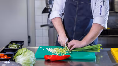 Op de linkerfoto een mooi opgemaakt bord met een gerecht dat bestaat uit onder andere aardappel en wortel. Op de rechterfoto snijdt een Paresto-keukenmedewerker een aantal lente-uitjes.