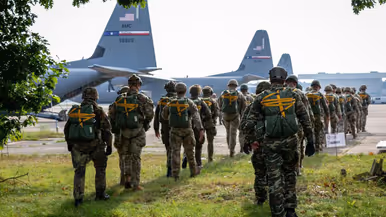 parachutisten lopen richting gereedstaande vliegtuigen. 