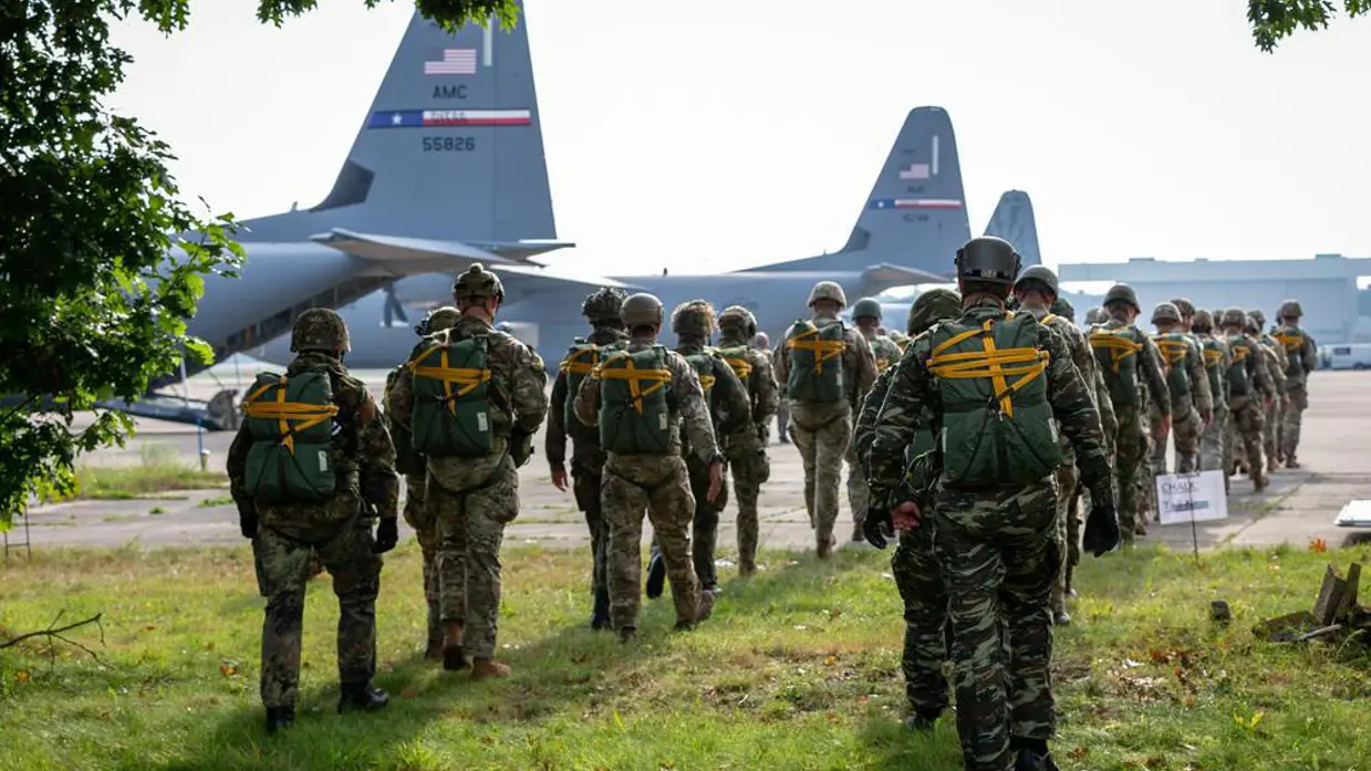 parachutisten lopen richting gereedstaande vliegtuigen. 