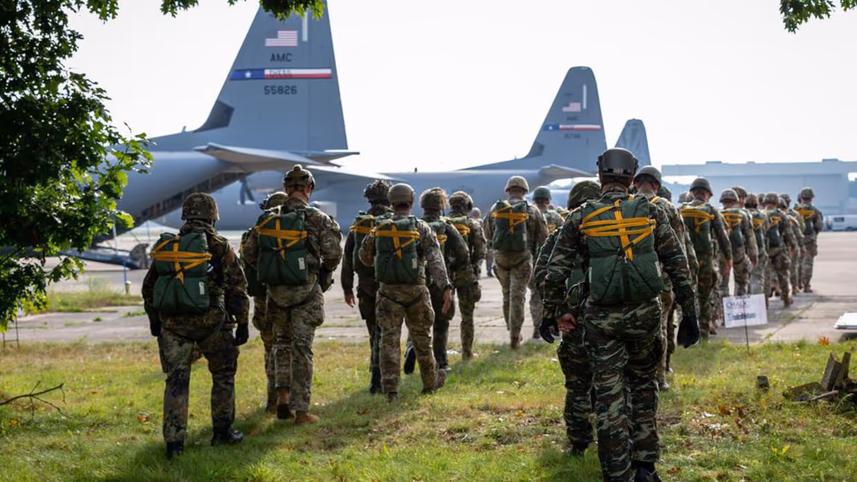 parachutisten lopen richting gereedstaande vliegtuigen. 