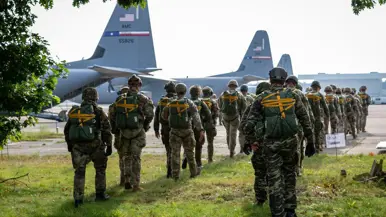 parachutisten lopen richting gereedstaande vliegtuigen. 