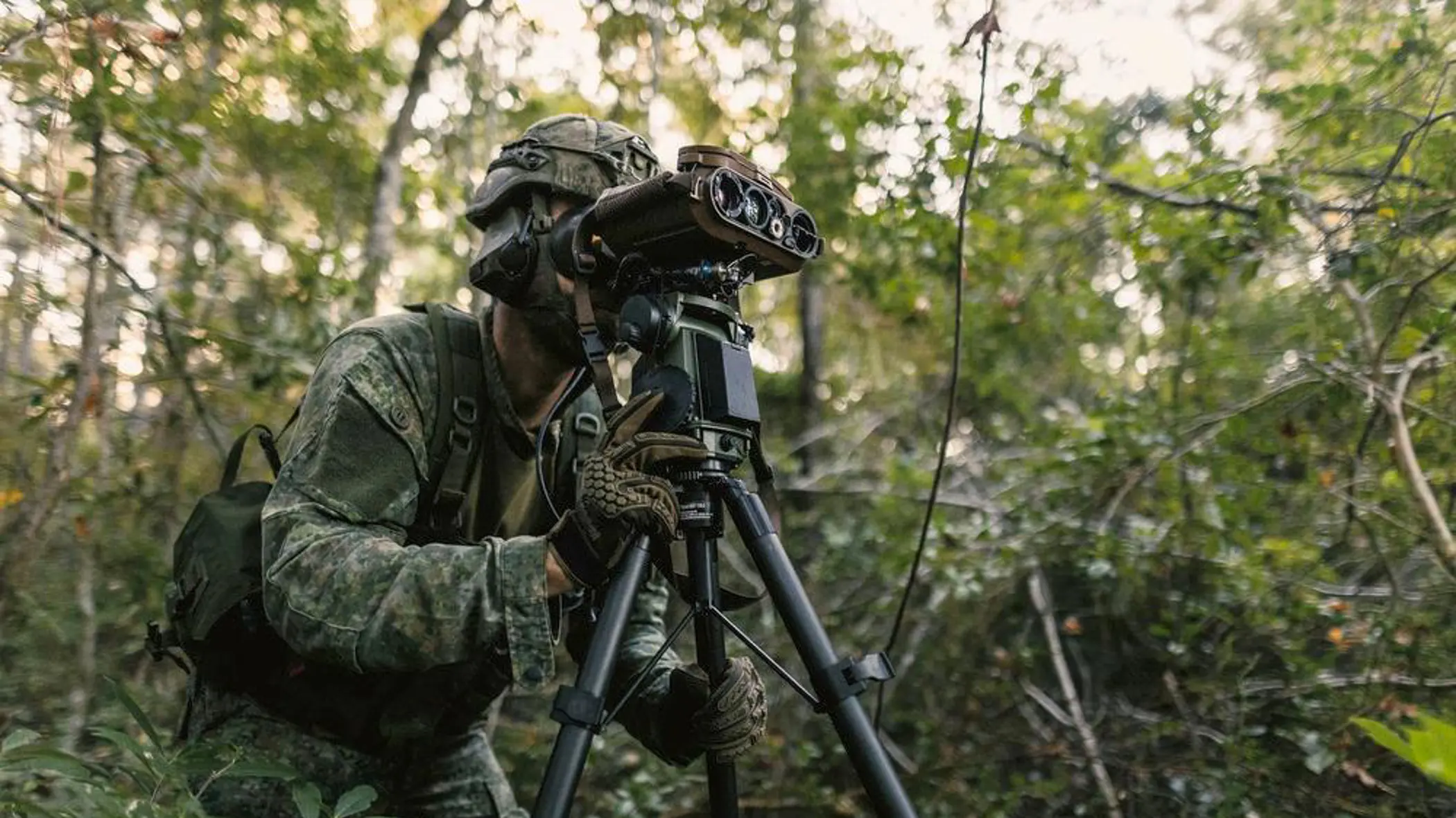 Een militair in gevechtstenue kijkt door een hypermoderne veldkijker die op een standaard staat.