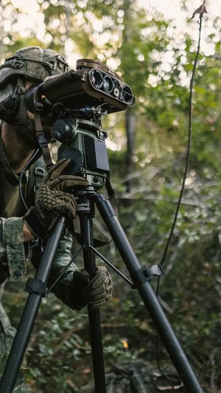 Een militair in gevechtstenue kijkt door een hypermoderne veldkijker die op een standaard staat.