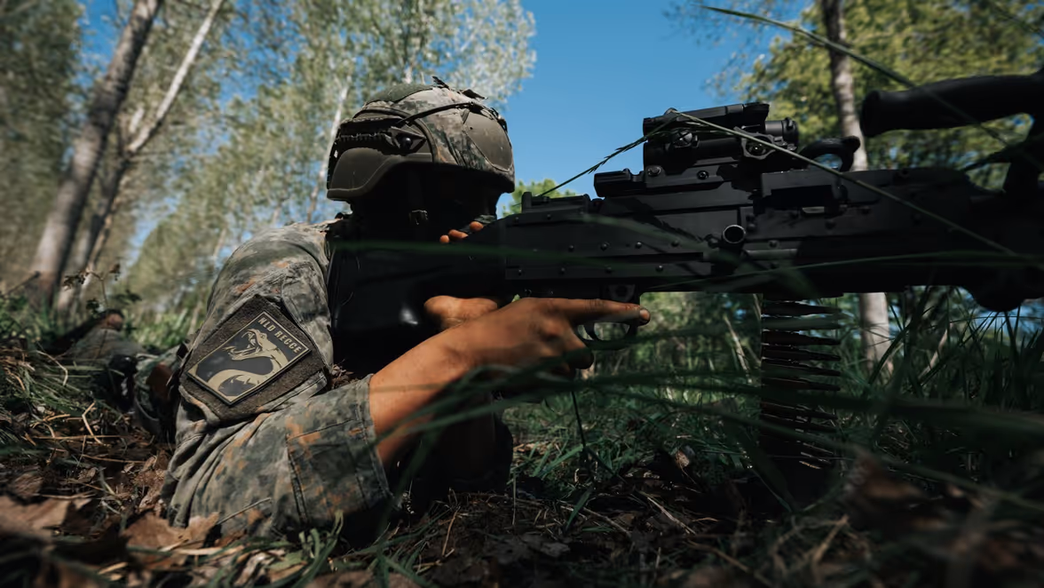 Een militair ligt op de grond met een vuurwapen in zijn handen. 