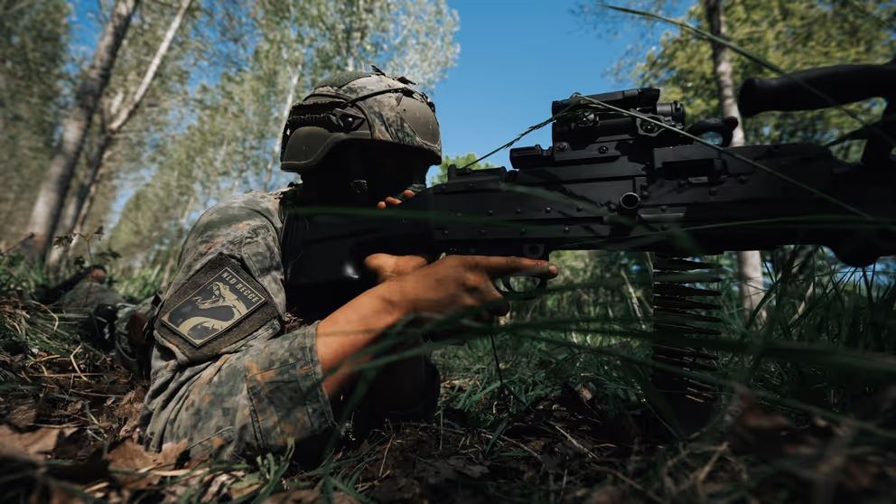 Een militair ligt op de grond met een vuurwapen. 