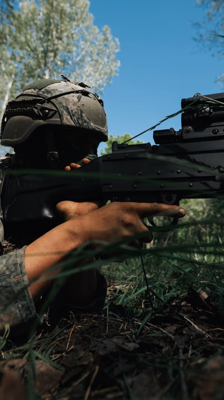 Een militair met een groot geweer in het bos. 