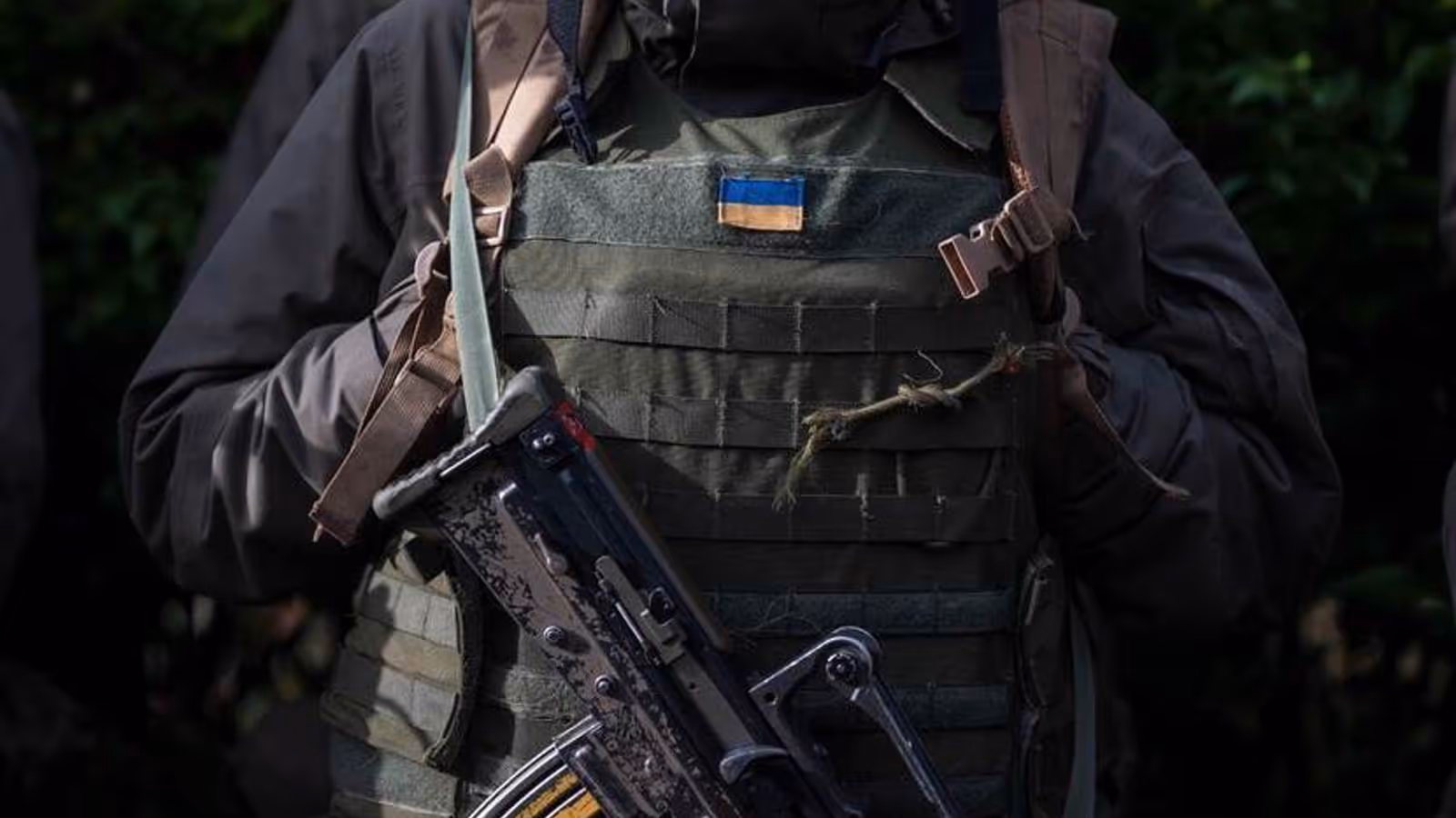 Vest van militair met Oekraïense vlag erop. Voor de borst hangt een machinegeweer.