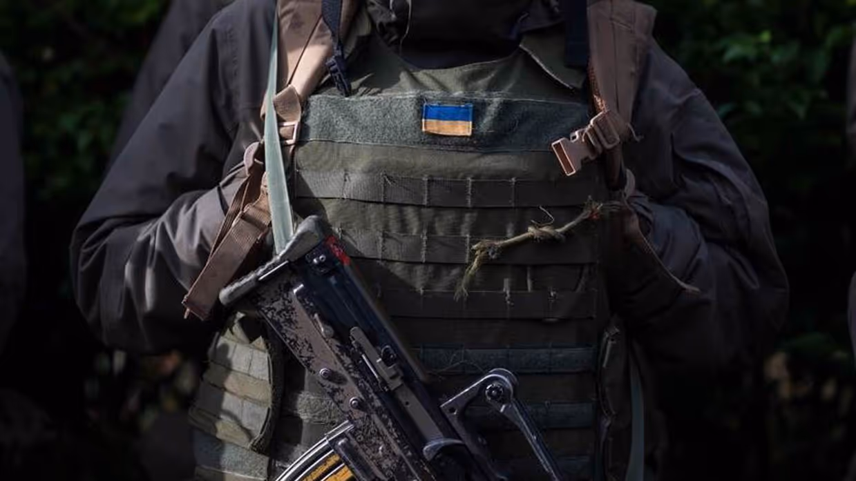 Vest van militair met Oekraïense vlag erop. Voor de borst hangt een machinegeweer.