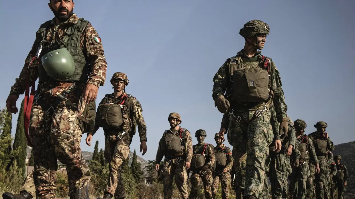  Italiaanse en Nederlandse militairen gekleed in gevechtstenue lopen in twee rijen.