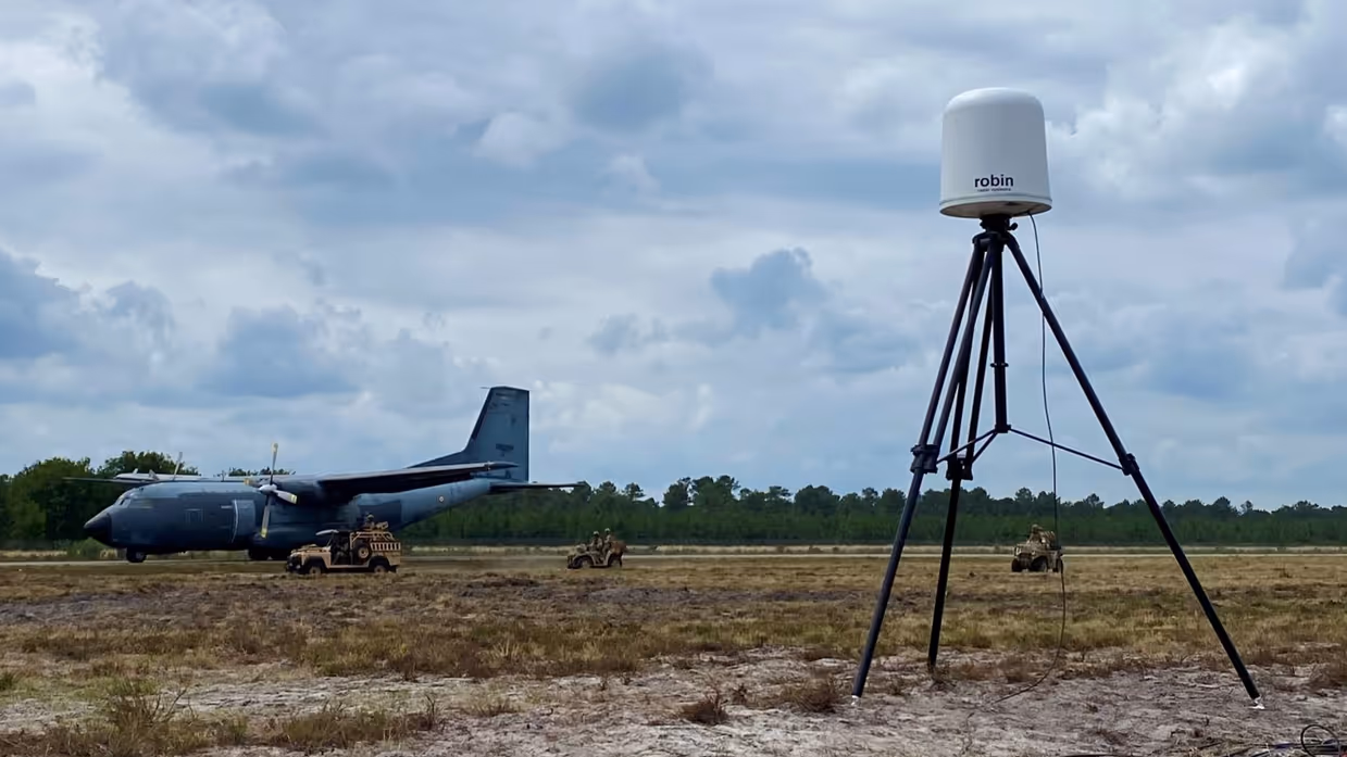  Een radarsysteem in een veld, daarachter een militair vliegtuig.