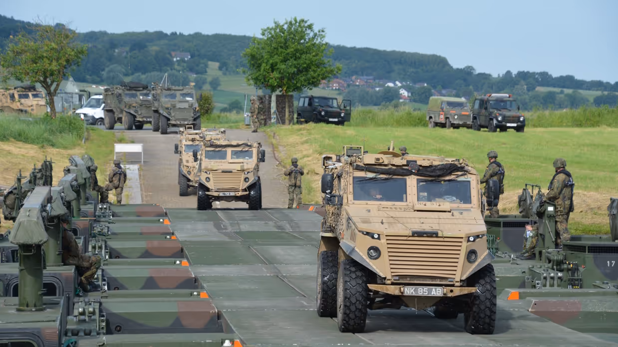 Militaire pantserwagens rijden op een landweg tussen bomen en andere voertuigen.