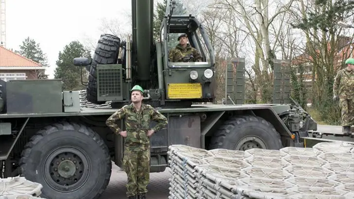 Onderkant van een stapel wegenmatten. De wegenmatten hangen aan een hijskraan.