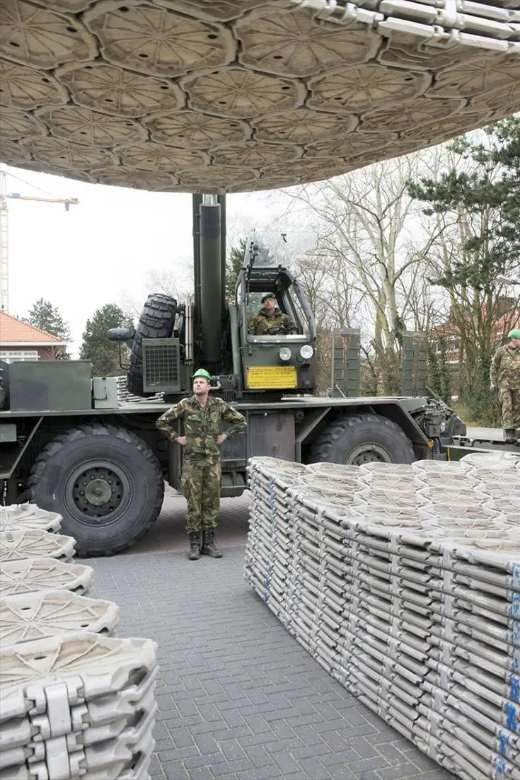 Onderkant van een stapel wegenmatten. De wegenmatten hangen aan een hijskraan.