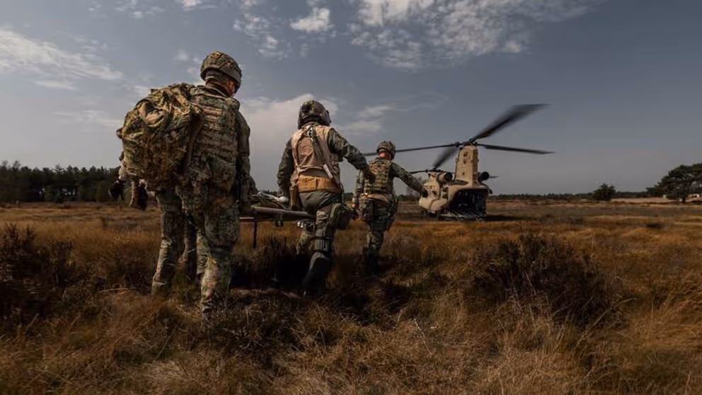 Militairen lopen met brancard naar Chinook-transporthelikopter.