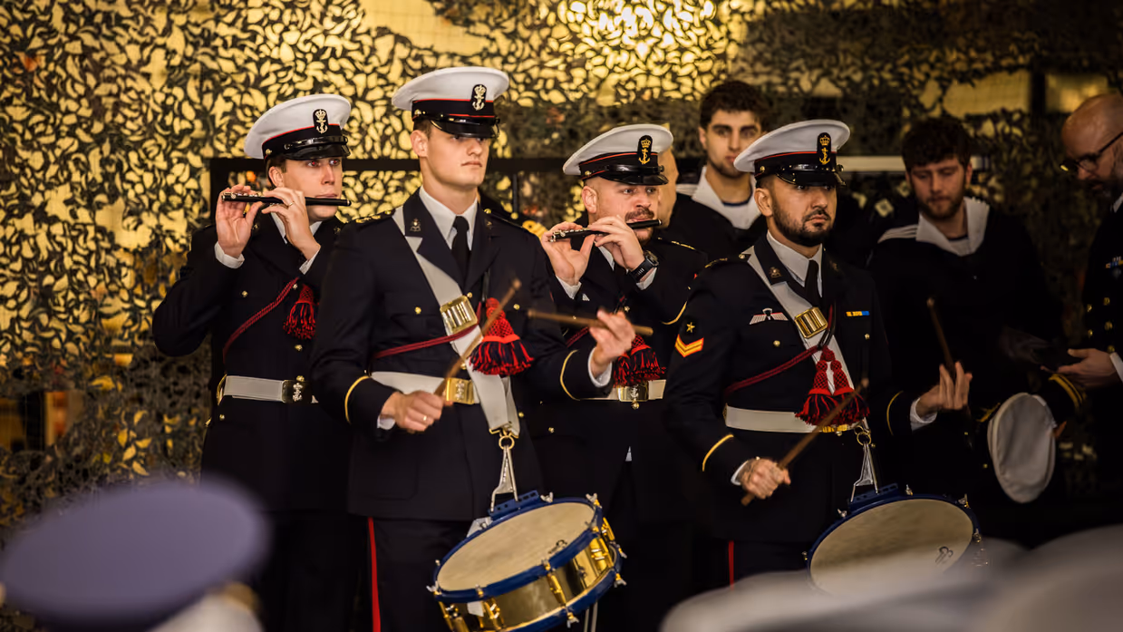 Mariniers die de muzikale omlijsting verzorgen met blaasinstrumenten en trommels.