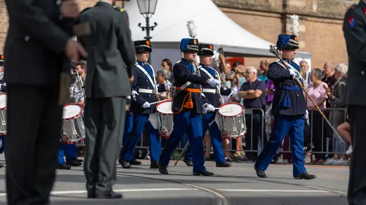 Militairen met muziekinstrument lopen mee in de stoet. 