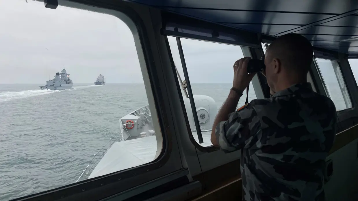 Een opvarende van het Ierse marineschip LE WIlliam Butler Yeats kijkt door een verrekijker naar de navigatieoefening..