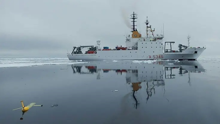 Een wit onderzoeksvaartuig op zee, met op de voorgrond een varende drone.