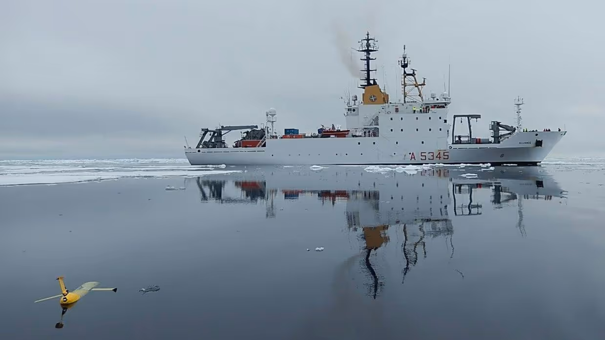 Een wit onderzoeksvaartuig op zee, met op de voorgrond een varende drone.