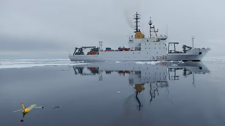 Een wit onderzoeksvaartuig op zee, met op de voorgrond een varende drone.