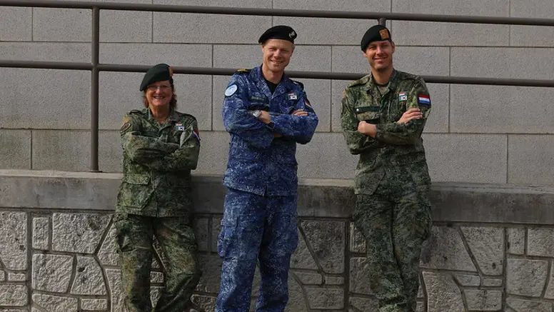 3 militairen kijken in de camera; 2 dragen een groen gevechtstenue, de middelste het boordtenue. 