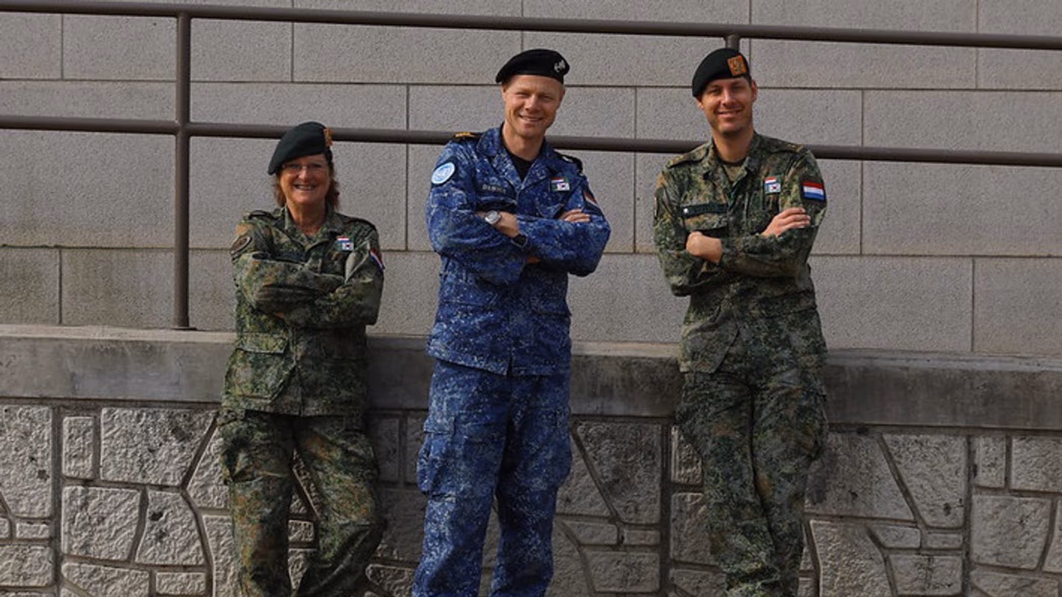 3 militairen kijken in de camera; 2 dragen een groen gevechtstenue, de middelste het boordtenue. 