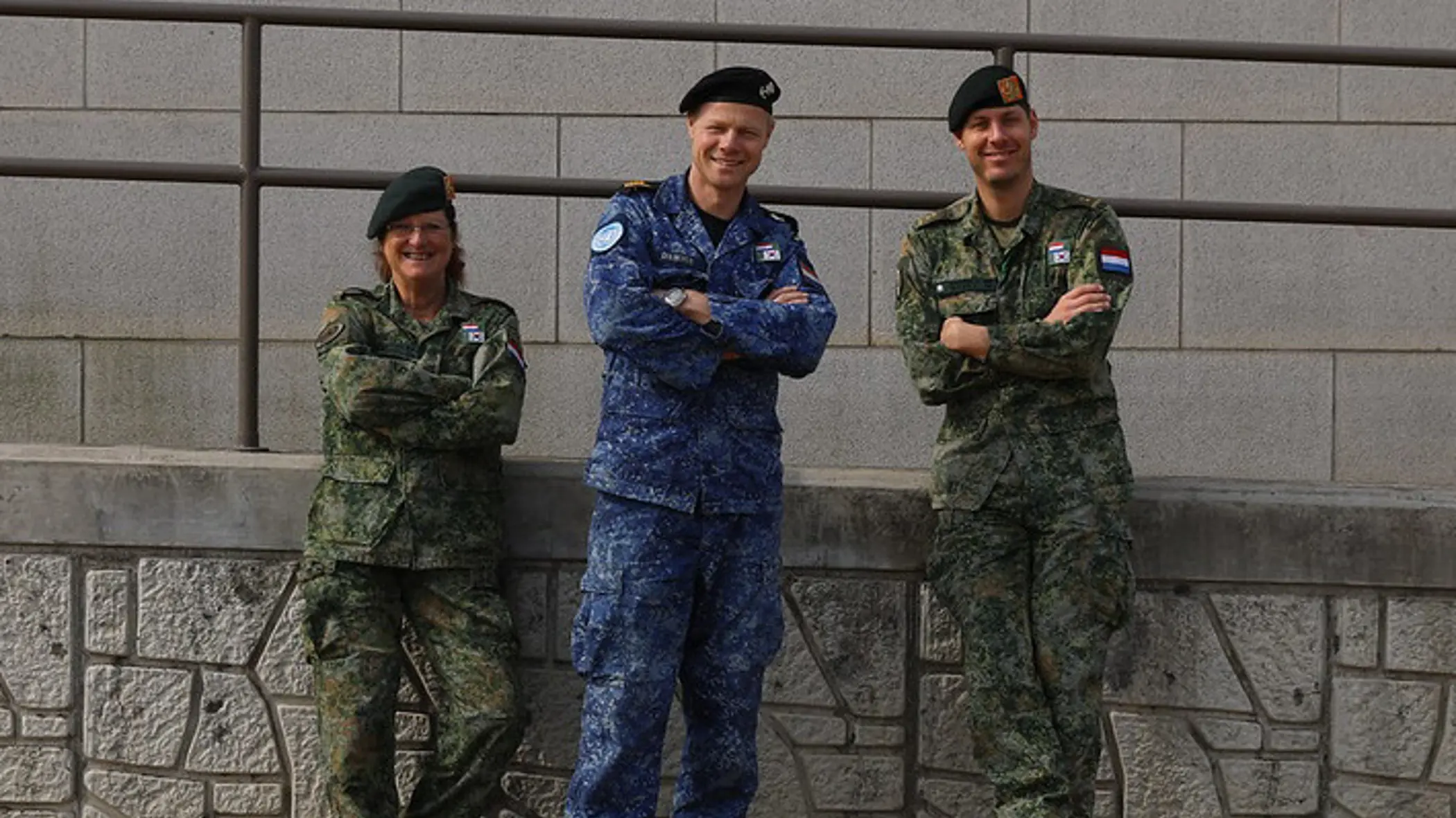3 militairen kijken in de camera; 2 dragen een groen gevechtstenue, de middelste het boordtenue. 