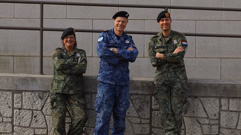 3 militairen kijken in de camera; 2 dragen een groen gevechtstenue, de middelste het boordtenue. 
