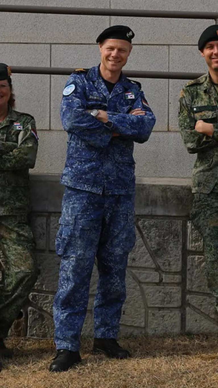 3 militairen kijken in de camera; 2 dragen een groen gevechtstenue, de middelste het boordtenue. 