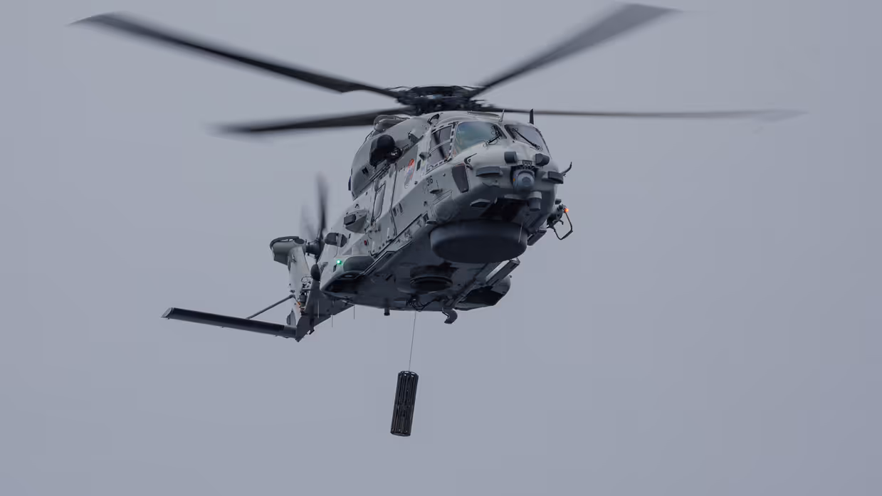 Links een NH90 maritieme helikopter met daaronder een sonar. 