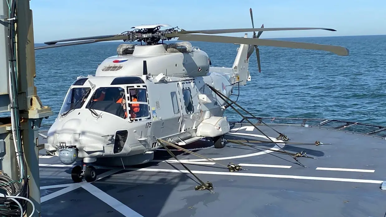 ALT-tekst: Een NH90 met banden vastgemaakt op een scheepsplatform van een schip op zee. 