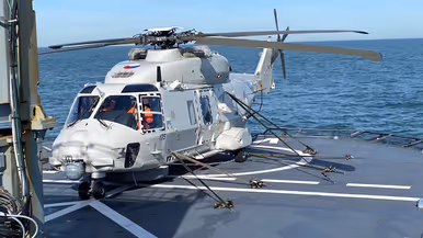 ALT-tekst: Een NH90 met banden vastgemaakt op een scheepsplatform van een schip op zee. 