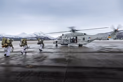 Mariniers lopen naar een NH90-helikopter. Op de achtergrond besneeuwde bergtoppen.