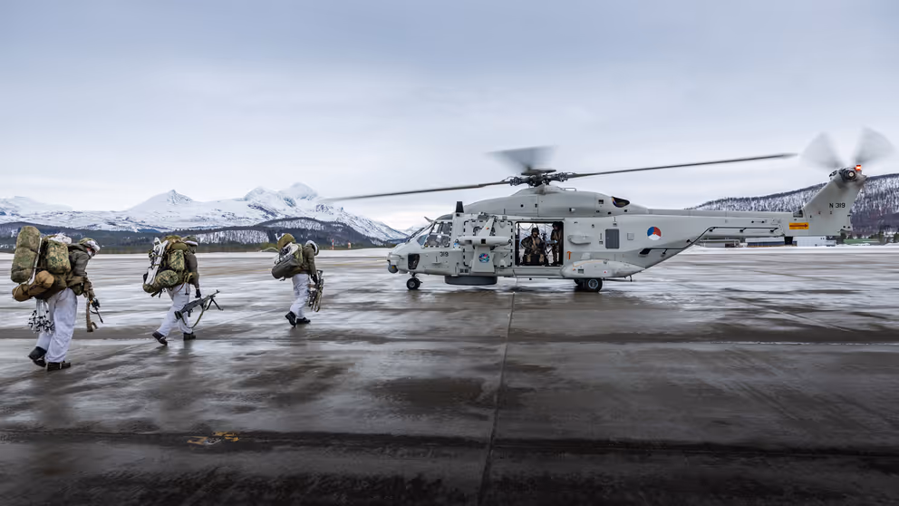 Mariniers lopen naar een NH90-helikopter. Op de achtergrond besneeuwde bergtoppen.