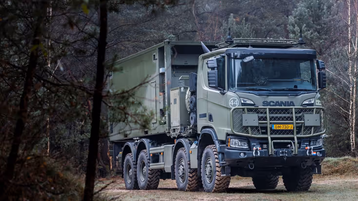 Een donkergroene Scania Gryphus-truck rijdt door een beboste omgeving. Achterop staat een container.