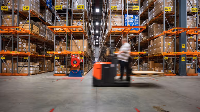 Een man rijdt op een voertuig door een opslagdepot.