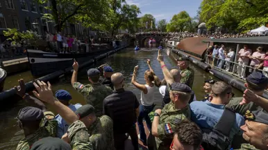 Een boot met dansende militairen vaart tijdens de Worldpride langs volgepakte grachten.