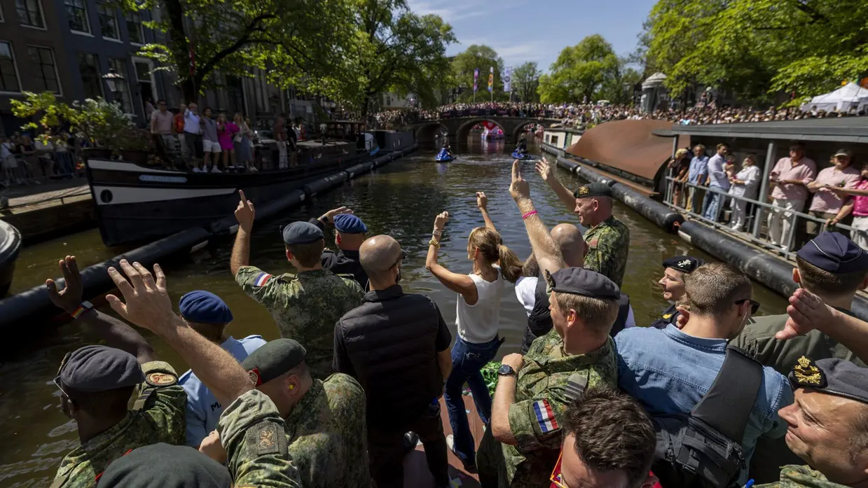 Een boot met dansende militairen vaart tijdens de Worldpride langs volgepakte grachten.