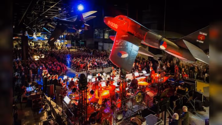 Overzicht van het podium met muzikanten en het publiek in het Nationaal Militair Museum. 