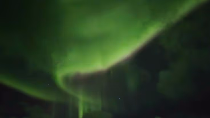 Groene slierten van het Noorderlicht in de nachtelijke hemel.