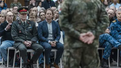  links: de staatssecretaris zit op een stoel. Rechts: Militairen lopen langs andere militairen
