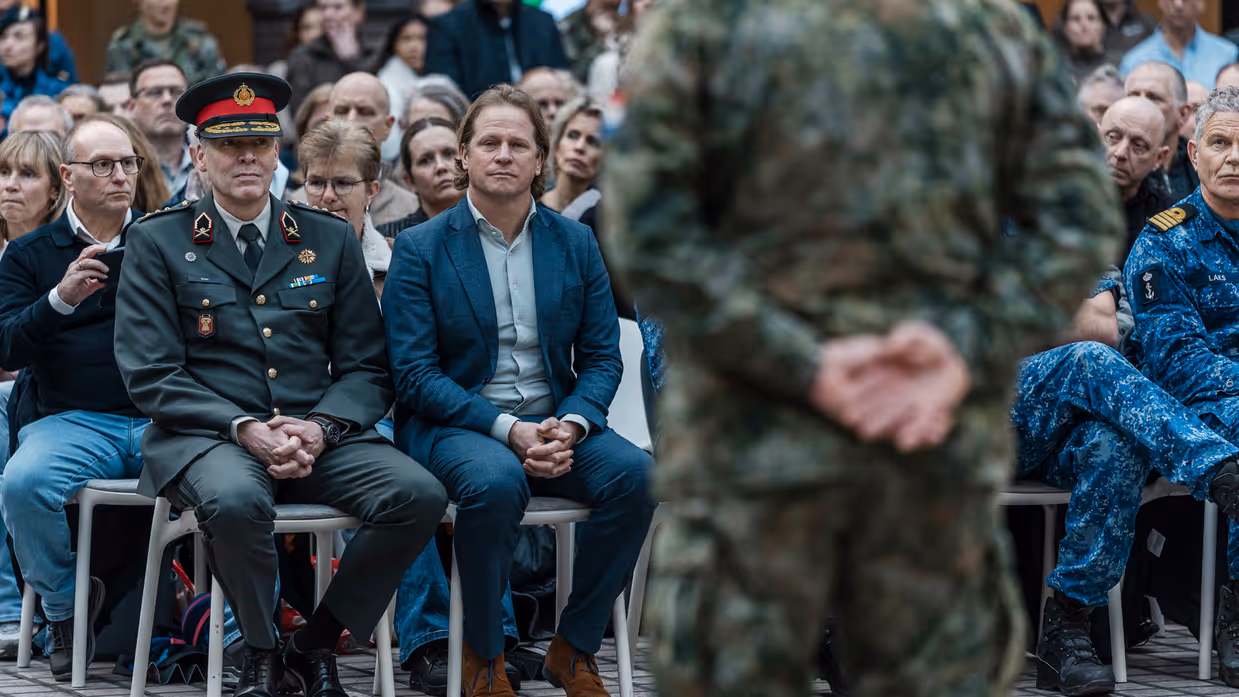 Staatssecretaris Gijs Tuinman zit op een stoel. Voor hem op de rug gezien een militair. 