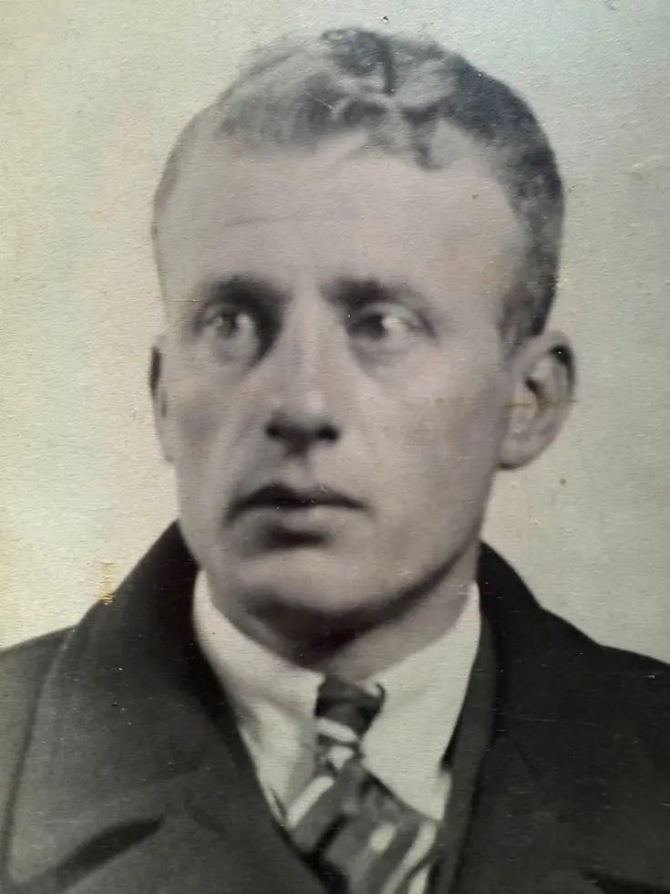 Een zwart-wit portret van een man met kort haar, een donker pak, witte overhemd en stropdas, tegen een lichte achtergrond.