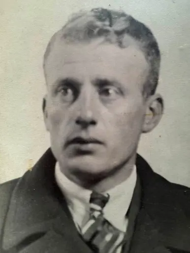 Een zwart-wit portret van een man met kort haar, een donker pak, witte overhemd en stropdas, tegen een lichte achtergrond.