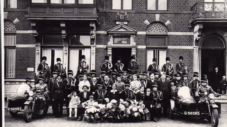Zwart-witgroepsfoto voor gebouw Koninklijke Marechaussee, inclusief paarden en zijspanmotoren.
